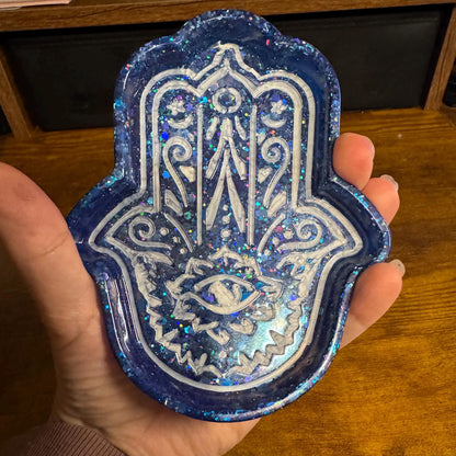 Hand holding a blue and white Hamsa hand patch on a wooden surface