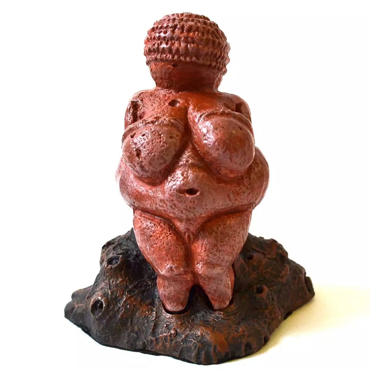 Venus of Willendorf replica statue: a red-brown figure with a banded head, rounded body, and arms across the breasts, standing on a dark rock-textured base.