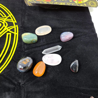 Variety of polished gemstones in different shapes and colors arranged on a black surface with a yellow circular pentagram design from the RWS tarot kit.