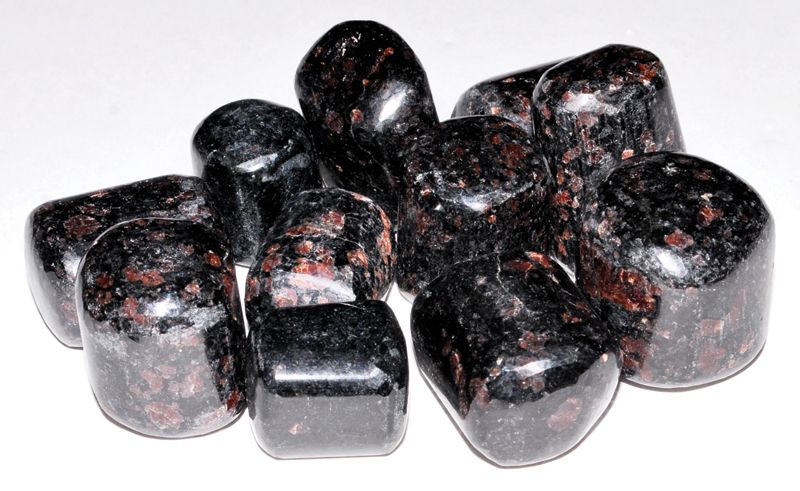 A pile of polished garnet in biotite tumbled stones showing deep red garnet crystals embedded in dark glittering mica matrix, sold in 1 lb bulk.
