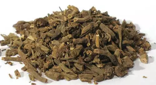 Valerian root cut dried herb in a pile on white surface, showing the fibrous tan-brown root pieces of Valeriana officinalis