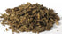 Valerian root cut dried herb in a pile on white surface, showing the fibrous tan-brown root pieces of Valeriana officinalis