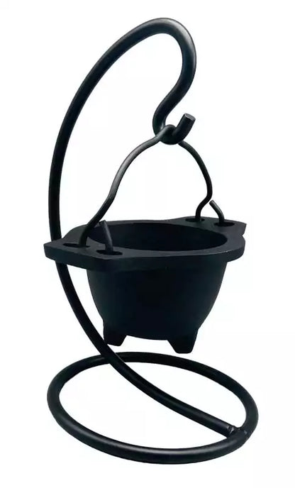 Hanging cast iron cauldron incense burner suspended on a decorative black metal stand — Gothic swinging cauldron design for altar smudging and resin work.