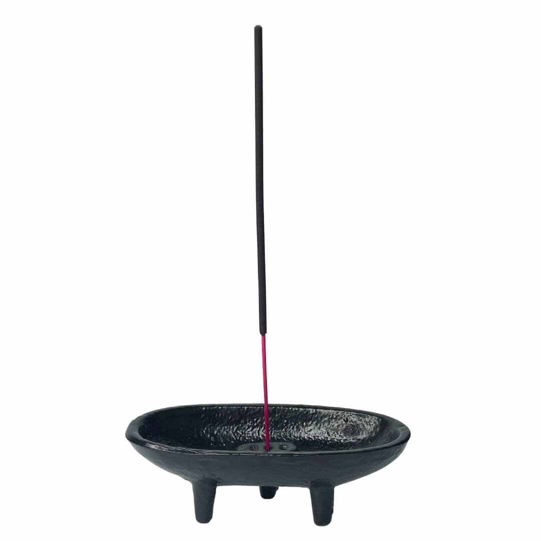 Black cast iron incense holder with a stick of incense burning — showing the cauldron burner in active ritual use.