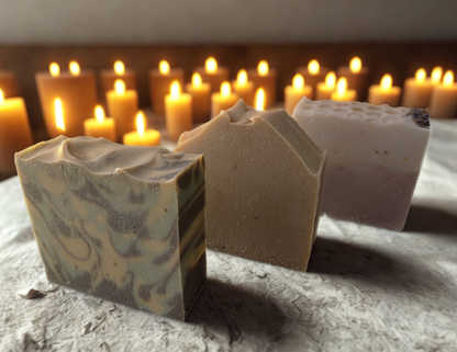 Three different soap bars from Grounding, Cleansing, and Protection collection with lit candles in background.