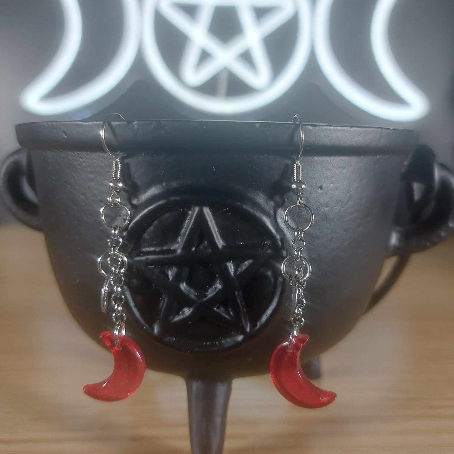 Red glass crescent moon dangle earrings with silver chains, displayed on a black cauldron.