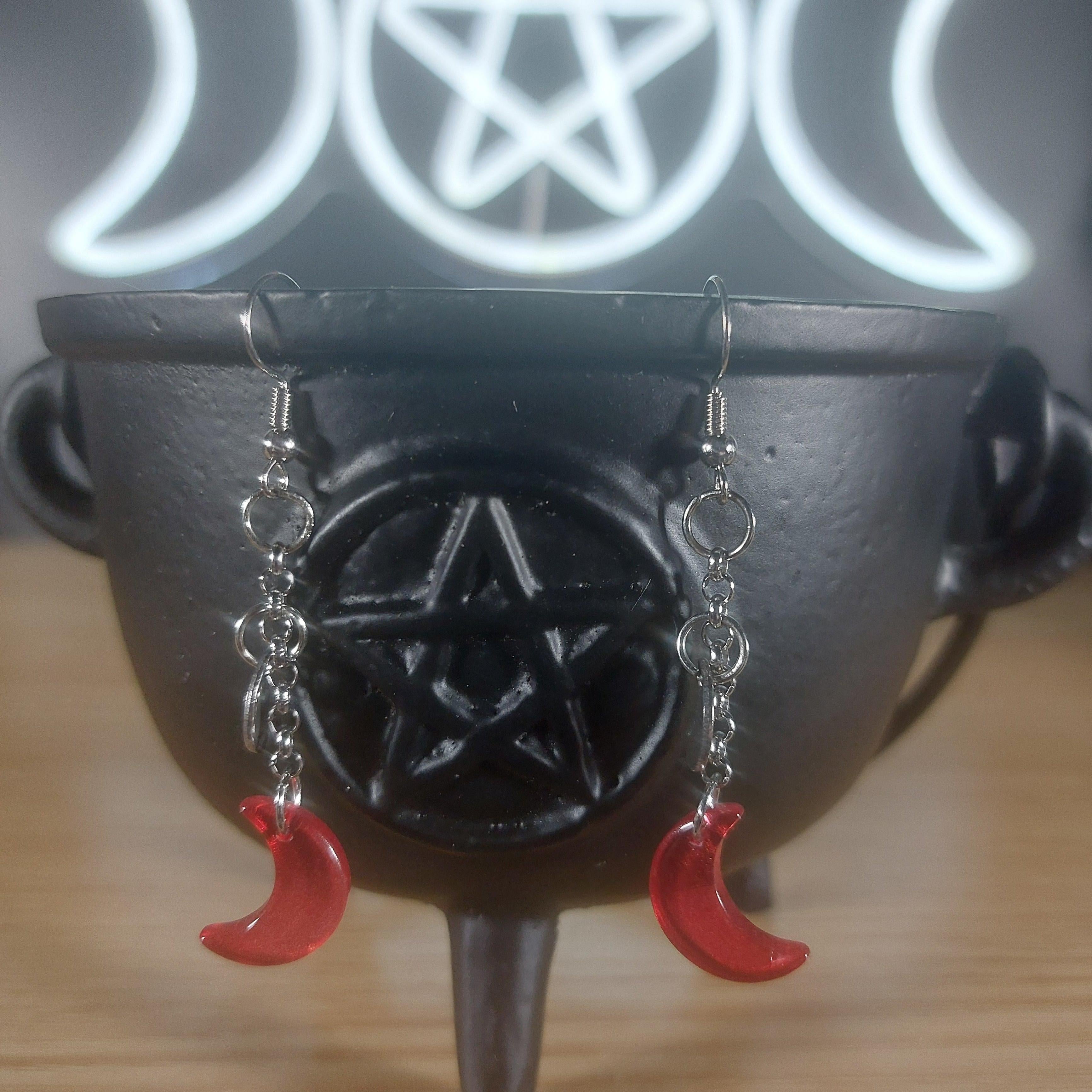 Red glass crescent moon dangle earrings with silver chains, displayed on a black cauldron.