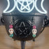 White howlite skull dangle earrings with pink and green glass beads on a black cauldron.