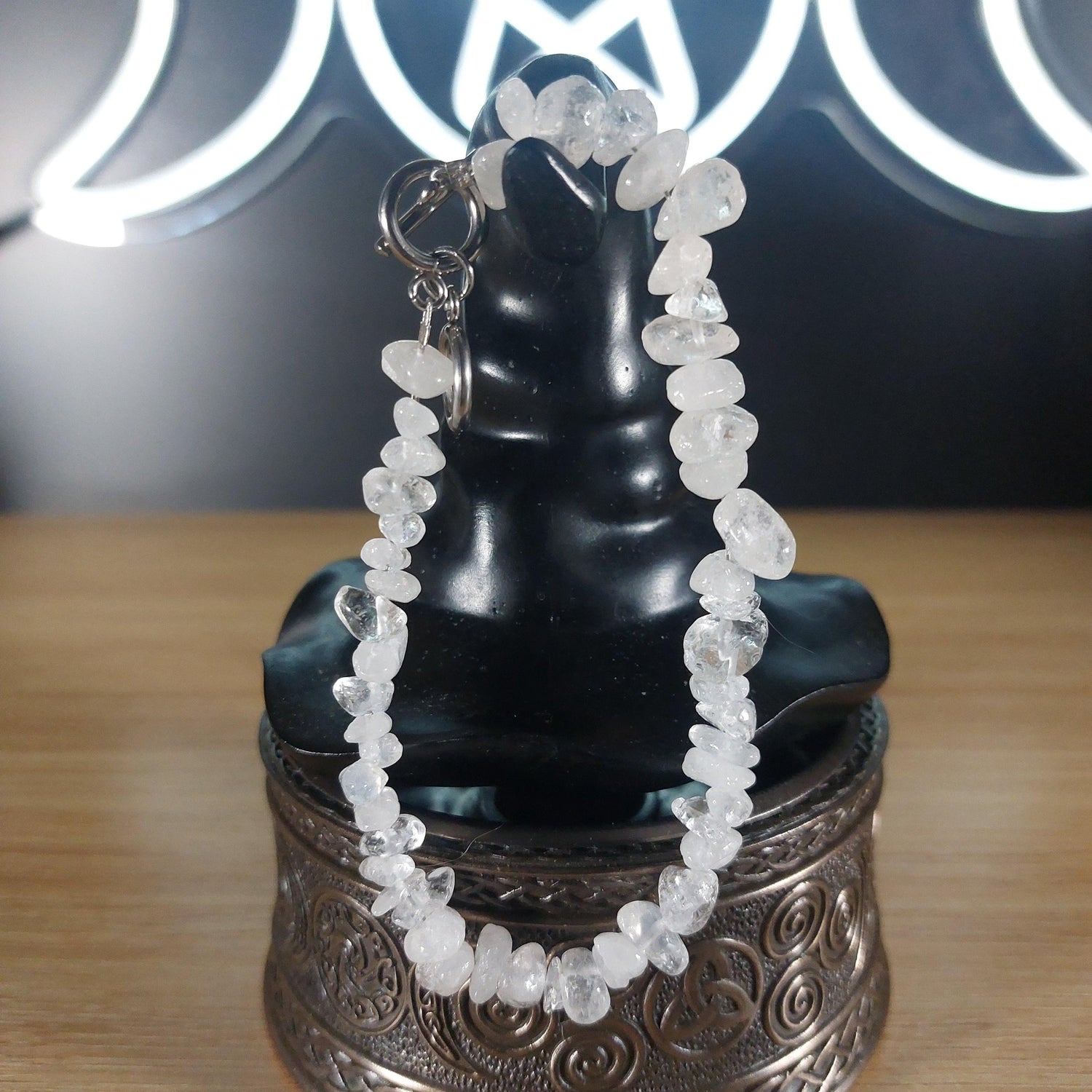Clear quartz crystal chip bracelet with stainless steel toggles on a black display stand.