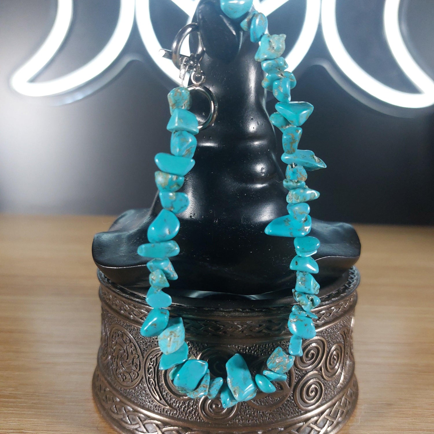 Turquoise crystal chip bracelet with a stainless steel toggle clasp, displayed on a black stand.