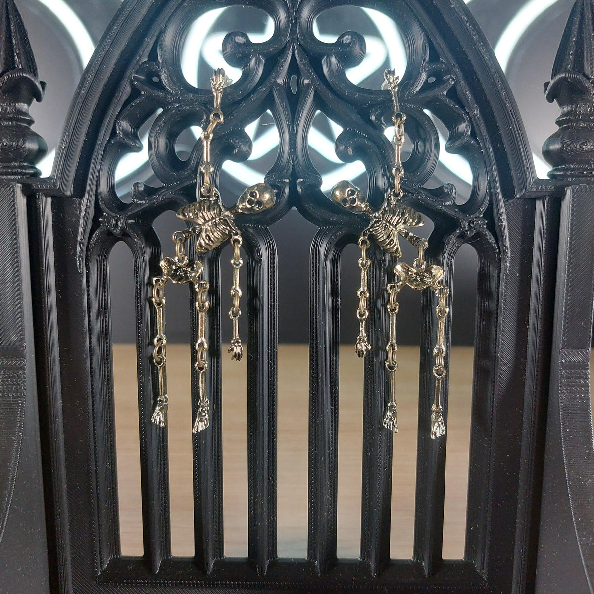 Antique gold tone skeleton dangle earrings on a black gothic arch display.