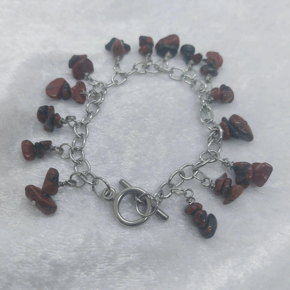 Mahogany obsidian chip bracelet with a stainless steel chain and toggle clasp on a white surface.