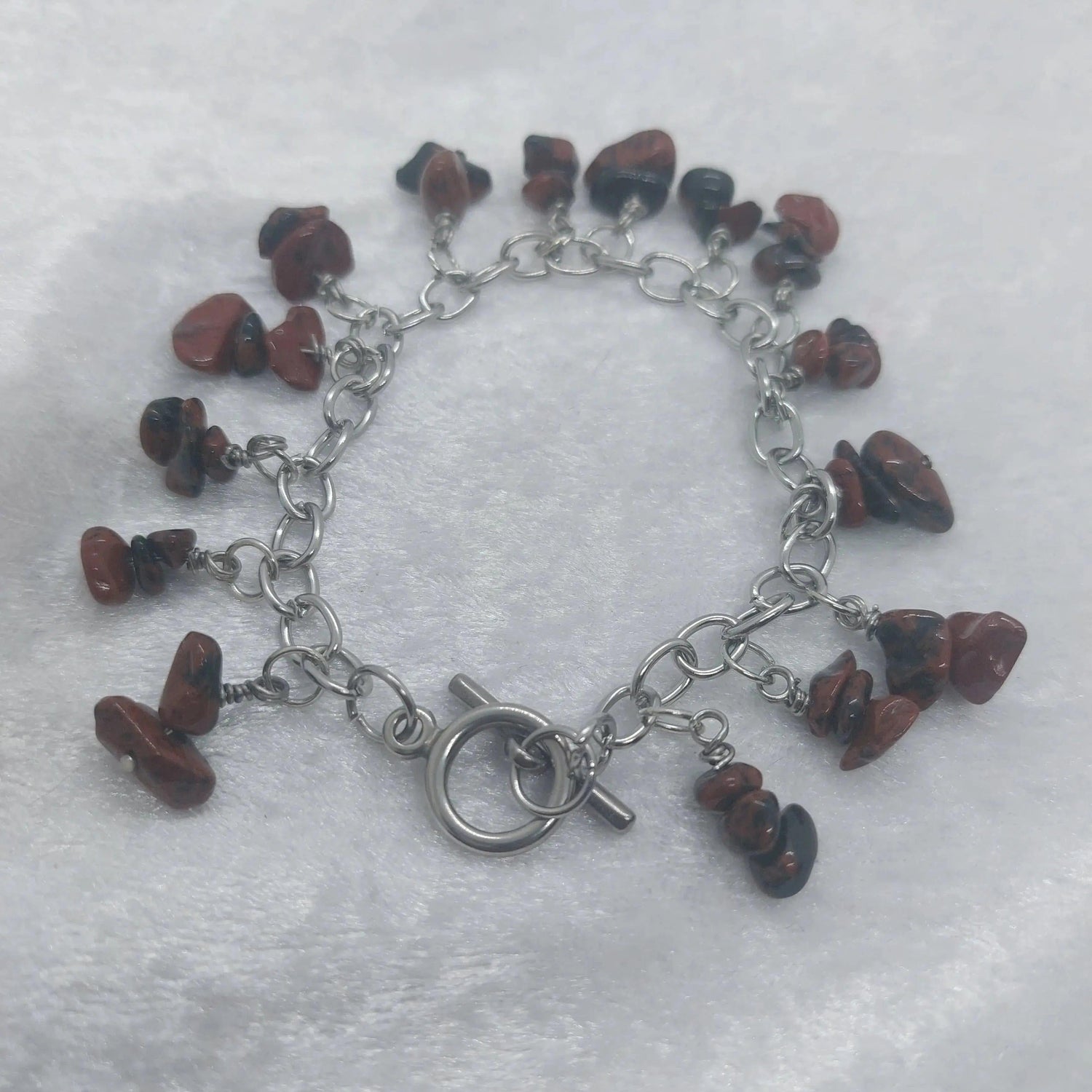 Mahogany obsidian chip bracelet with a stainless steel chain and toggle clasp on a white surface.