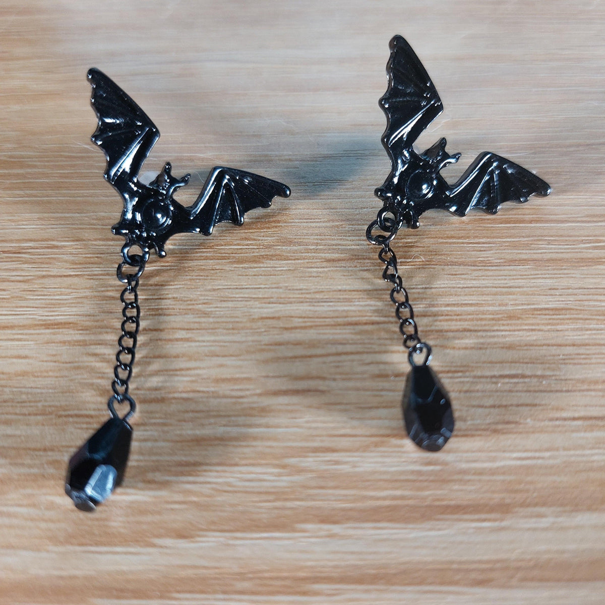 Pair of black metal bat stud earrings with dangling chains and teardrop gems.