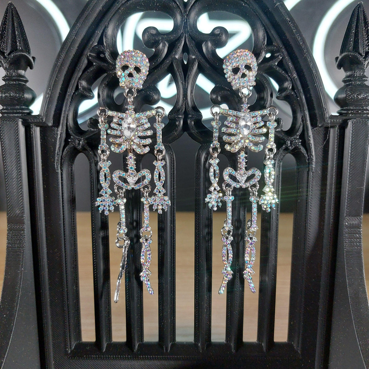Sparkling rhinestone skeleton dangle earrings on a black gothic stand.