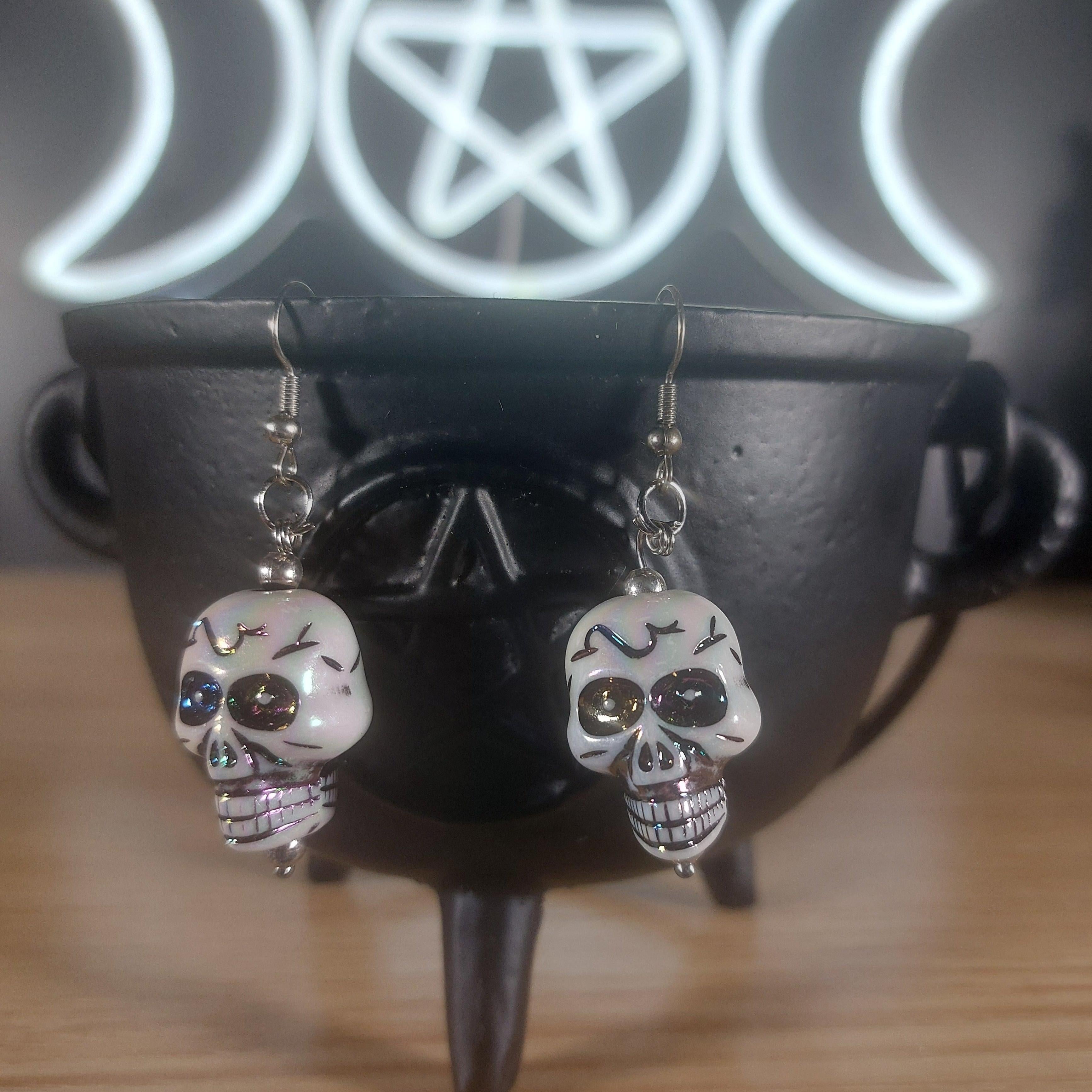 White plastic skull dangle earrings with rainbow accents, hanging from silver hooks.