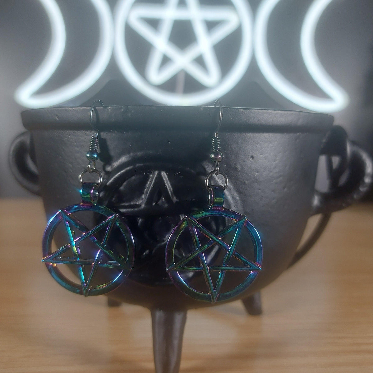 Rainbow iridescent inverted pentagram dangle earrings on a black cauldron.