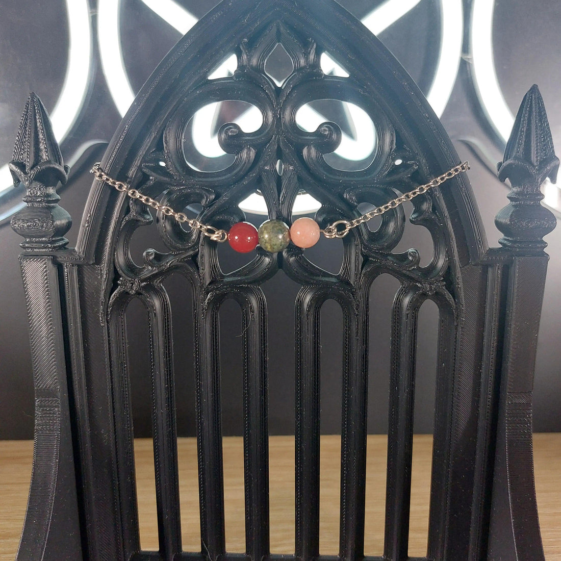 Aries power stone bracelet with red, green, and pink beads on a silver chain, displayed on a black gothic stand.