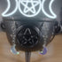 Iridescent clear glass moon dangle earrings hanging from a black cauldron with a pentagram.