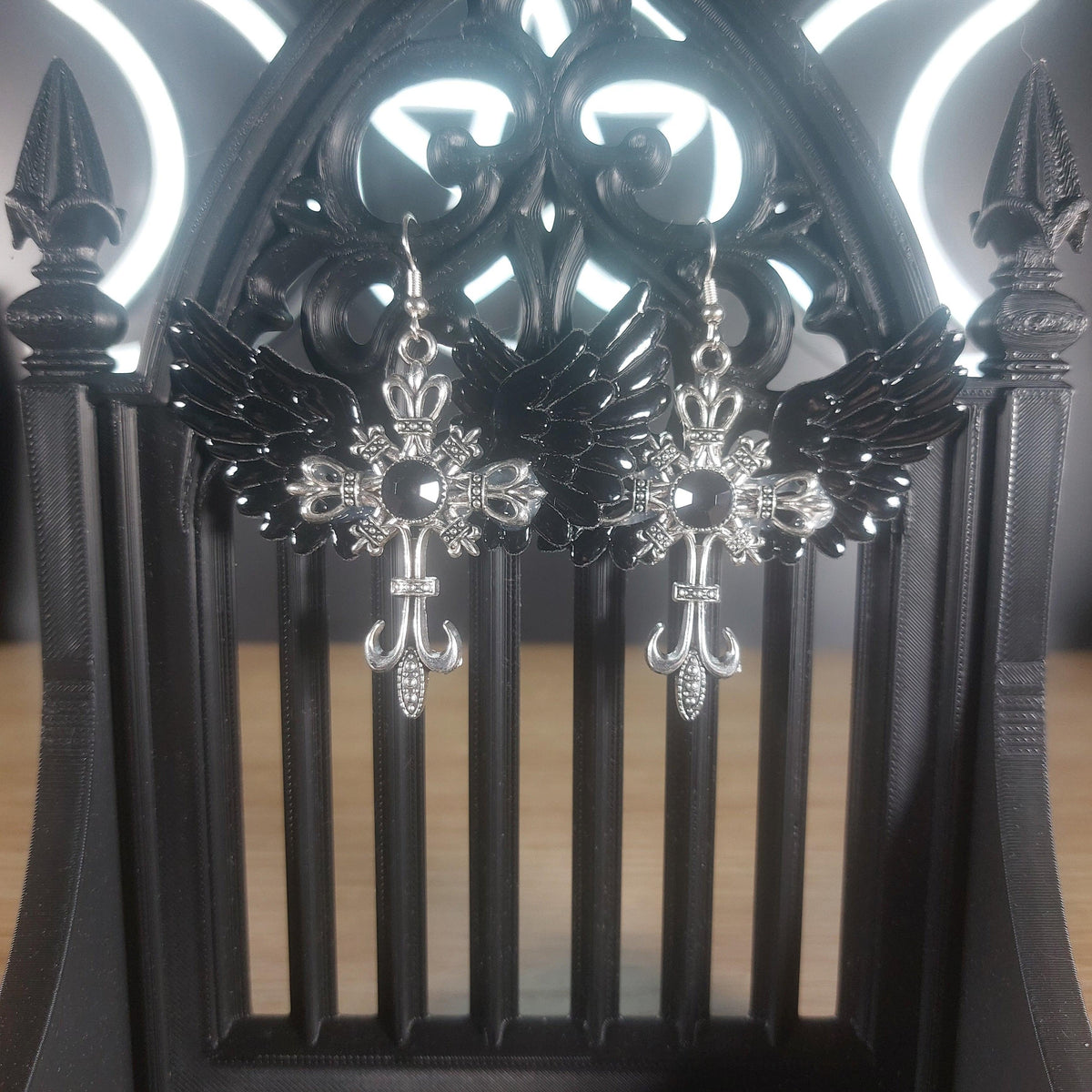 Black winged silver-tone cross dangle earrings with intricate gothic details.