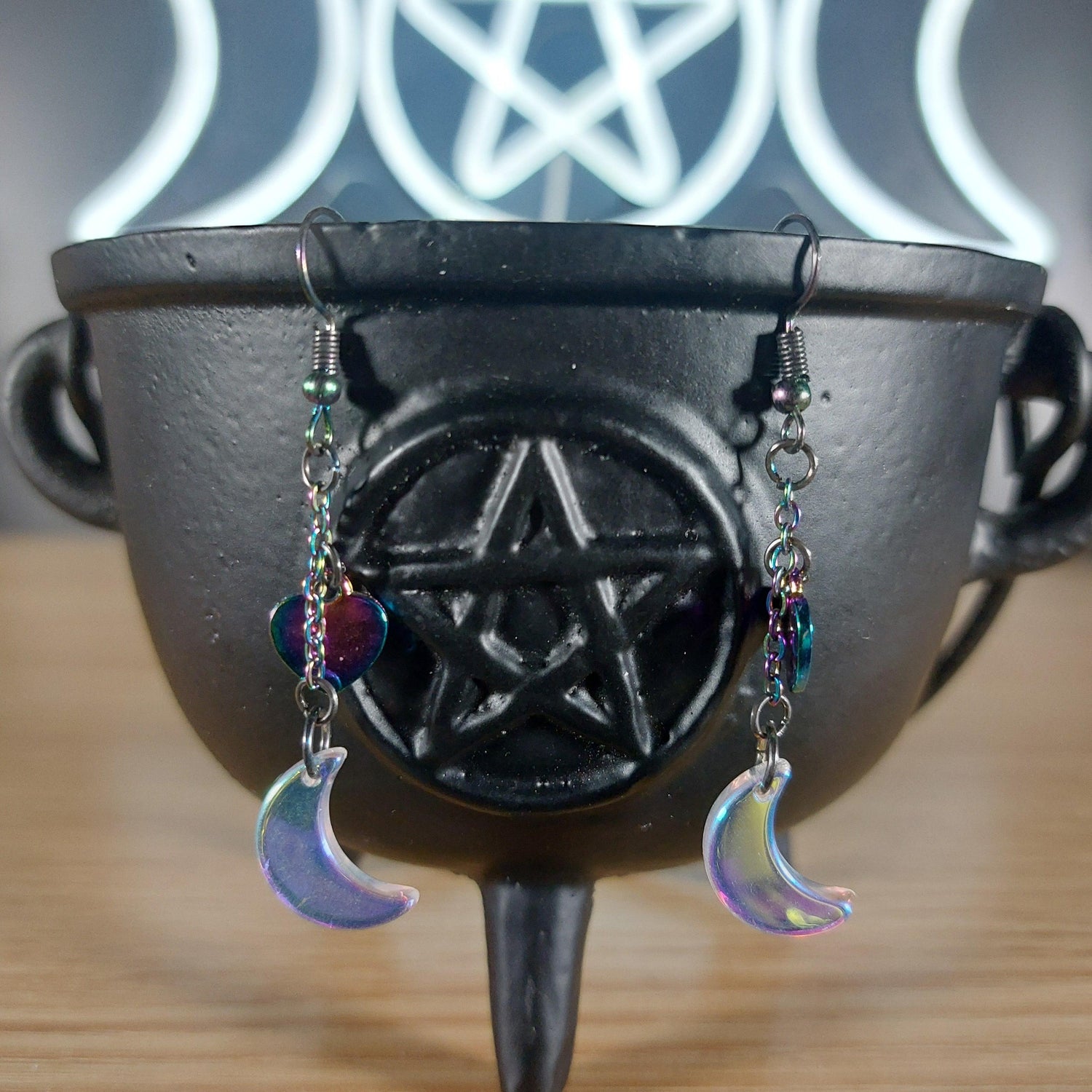 Iridescent glass moon earrings with rainbow chain and heart charms on a black cauldron.