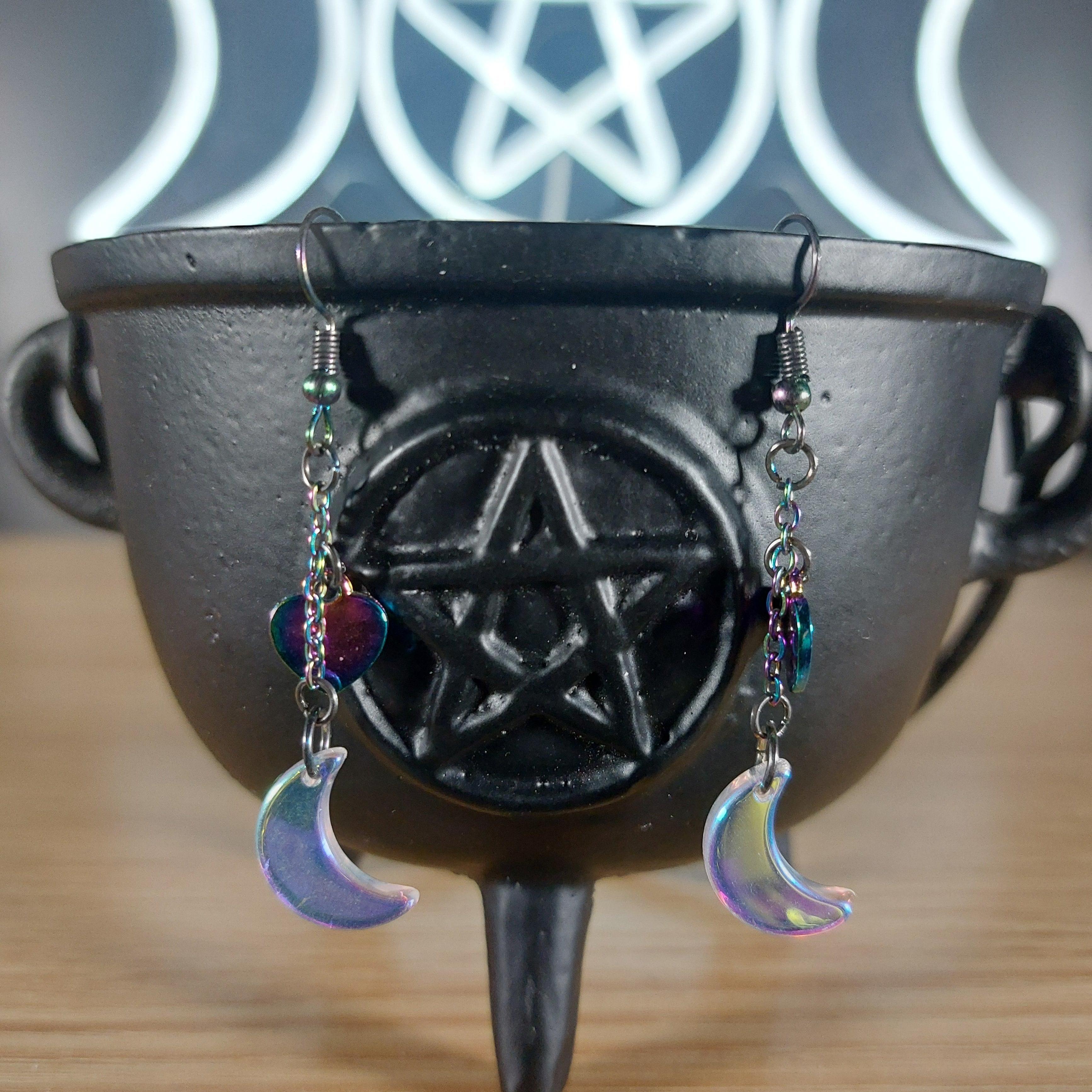 Iridescent glass moon earrings with rainbow chain and heart charms on a black cauldron.
