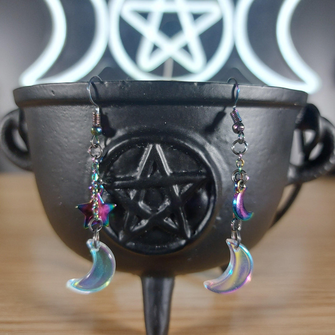 Iridescent glass moon and rainbow star dangle earrings on a black cauldron.