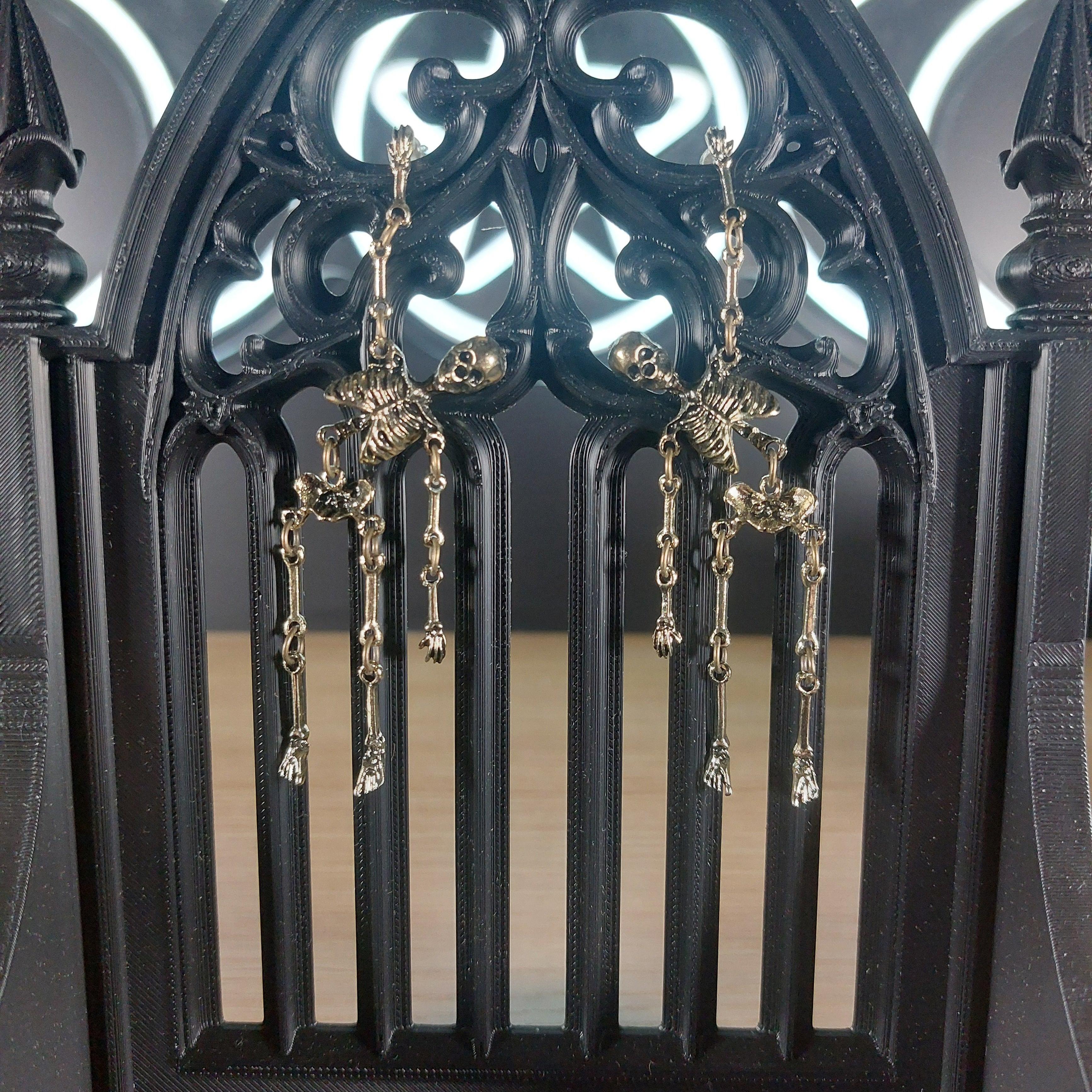 Antique gold tone skeleton dangle earrings on a black gothic arch display.