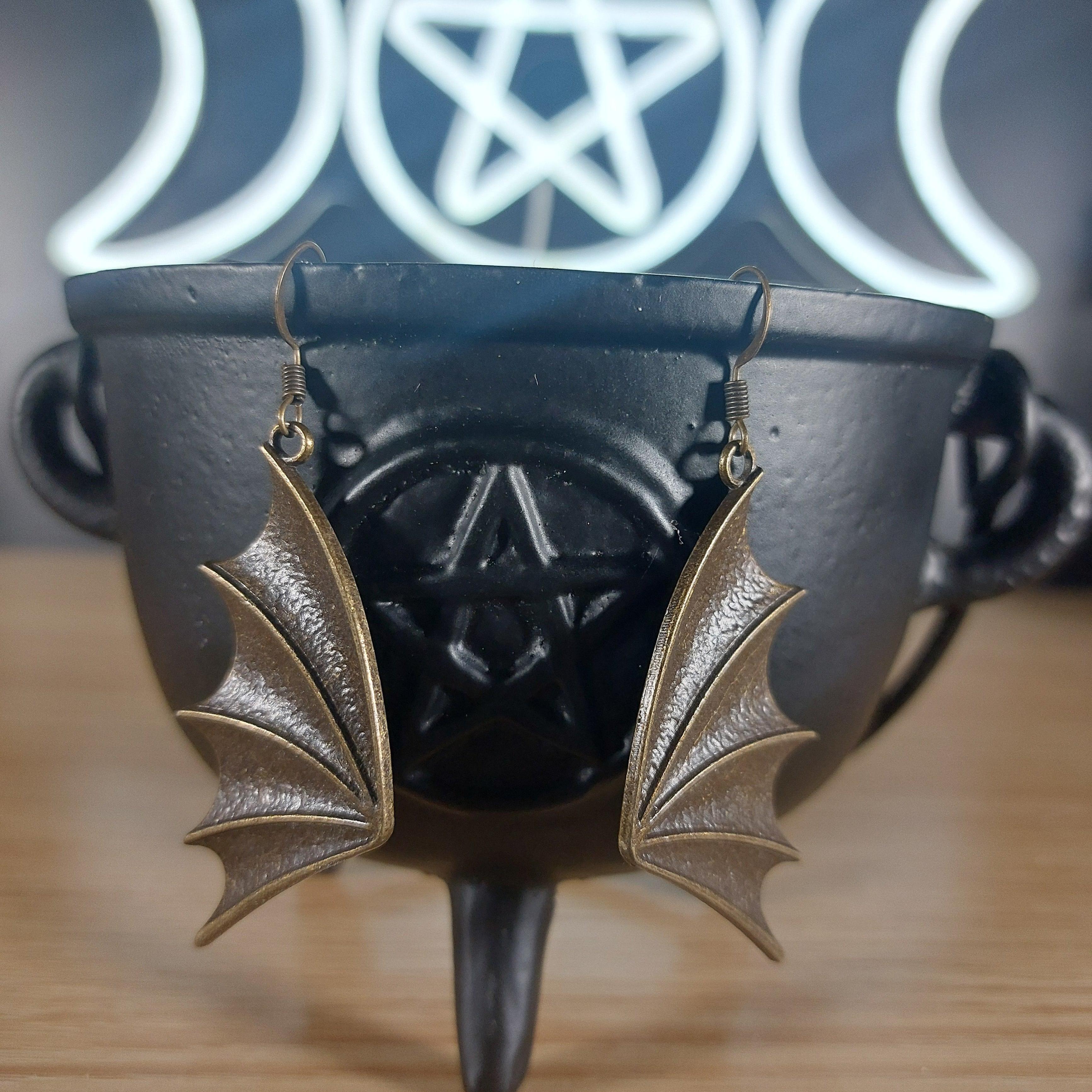 Bronze dragon wing dangle earrings hanging from a black cauldron with a pentagram.