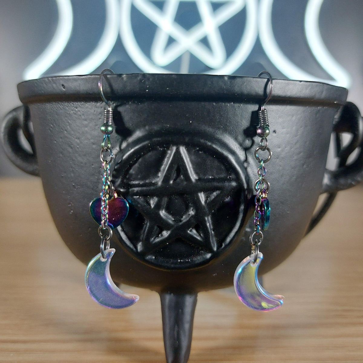 Iridescent glass moon earrings with rainbow chain and heart charms on a black cauldron.