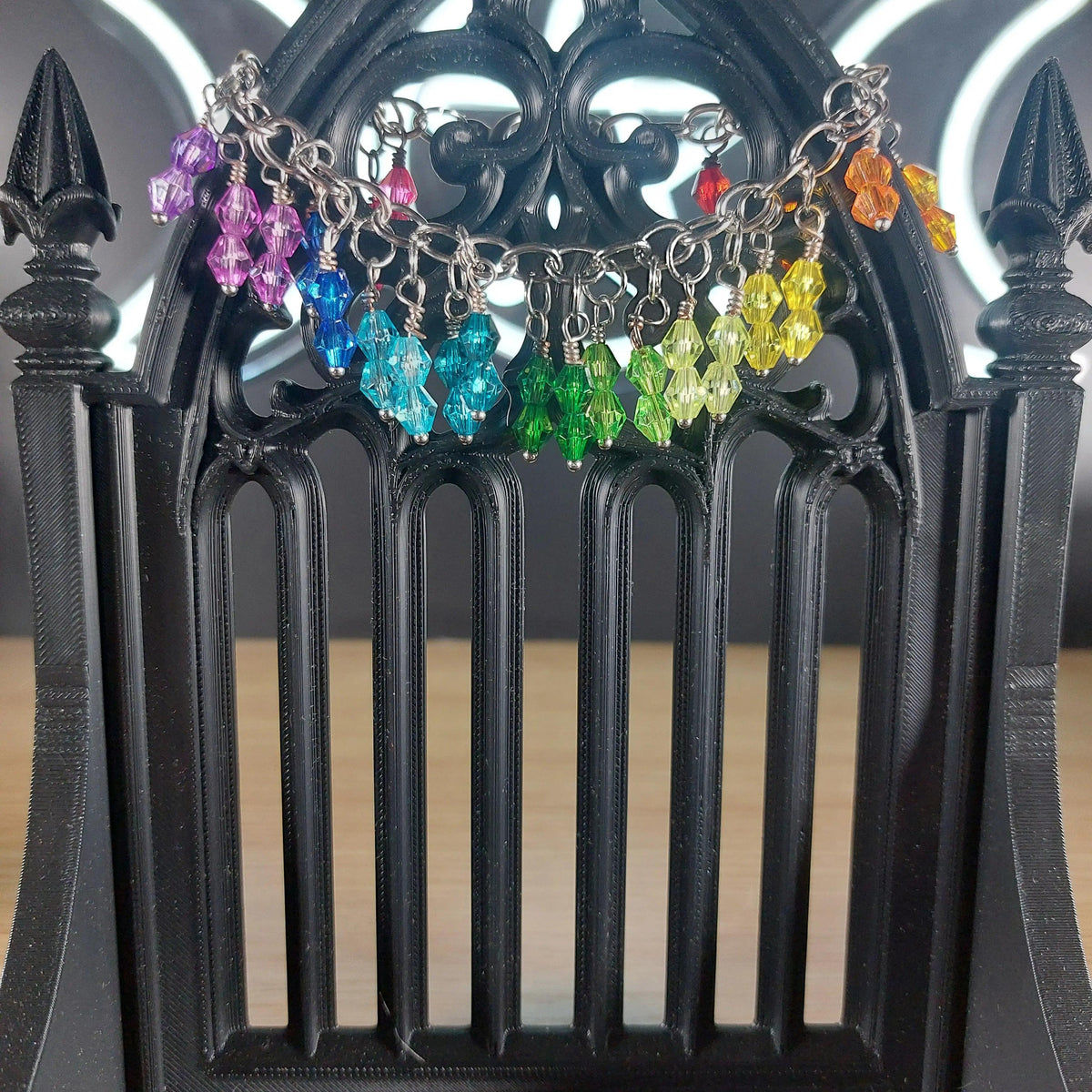 Rainbow bicone beaded bracelet with stainless steel chain, displayed on a black gothic stand.