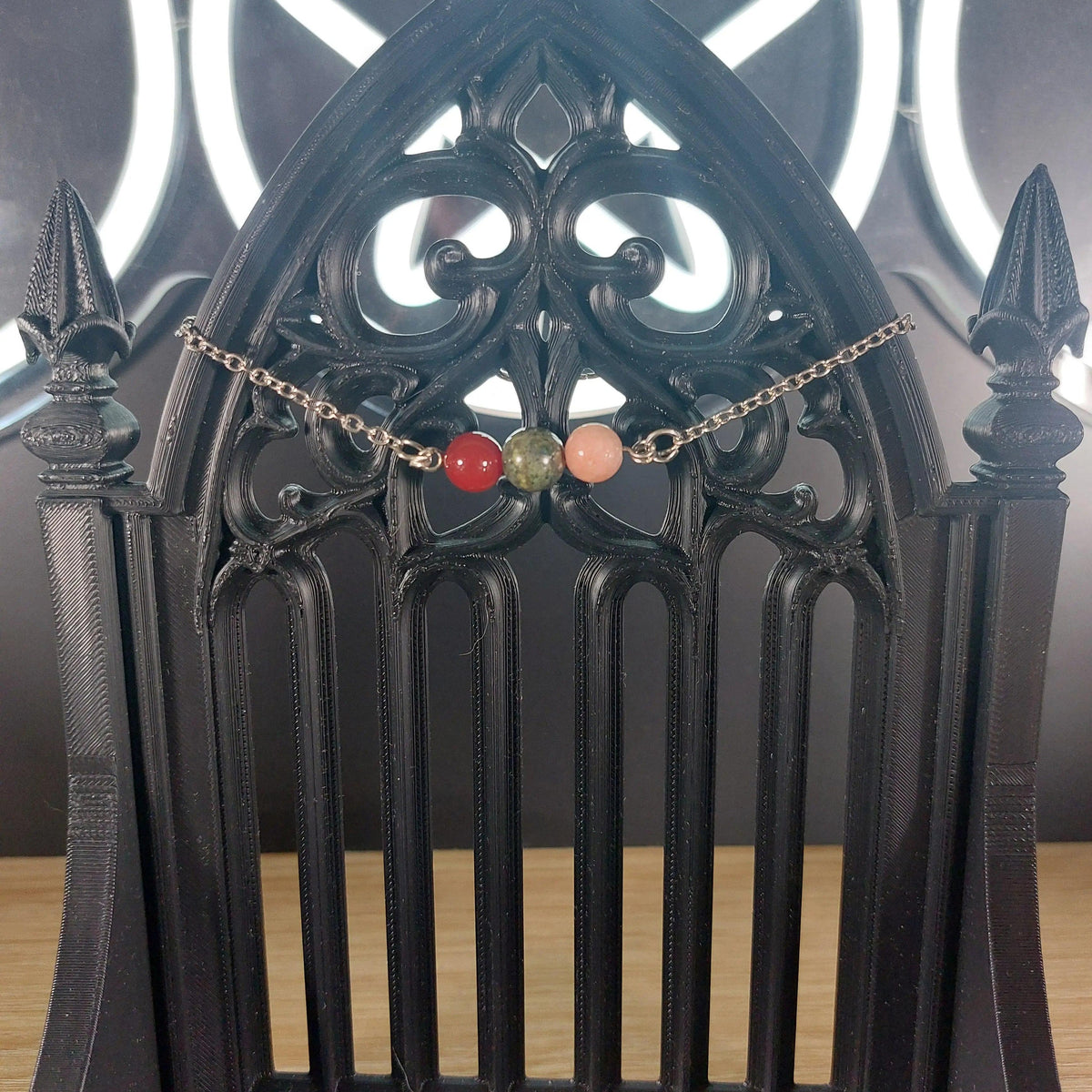 Aries power stone bracelet with red, green, and pink beads on a silver chain, displayed on a black gothic stand.