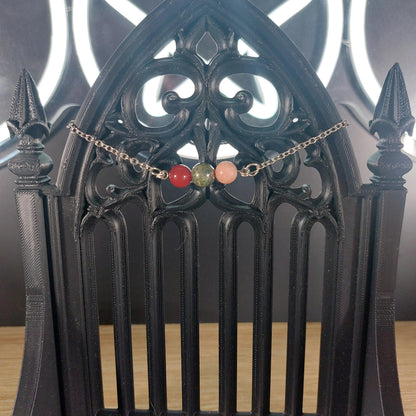 Aries power stone bracelet with red, green, and pink beads on a silver chain, displayed on a black gothic stand.