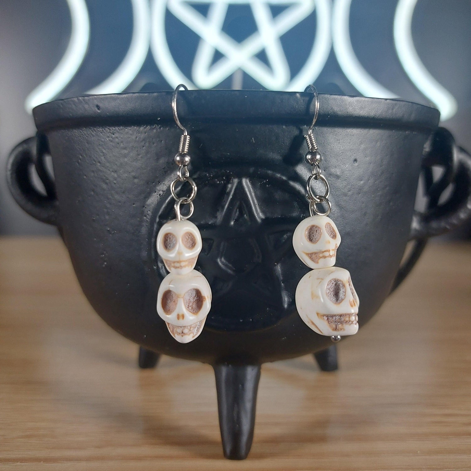 White howlite crystal skull 2-tier dangle earrings on a black cauldron.