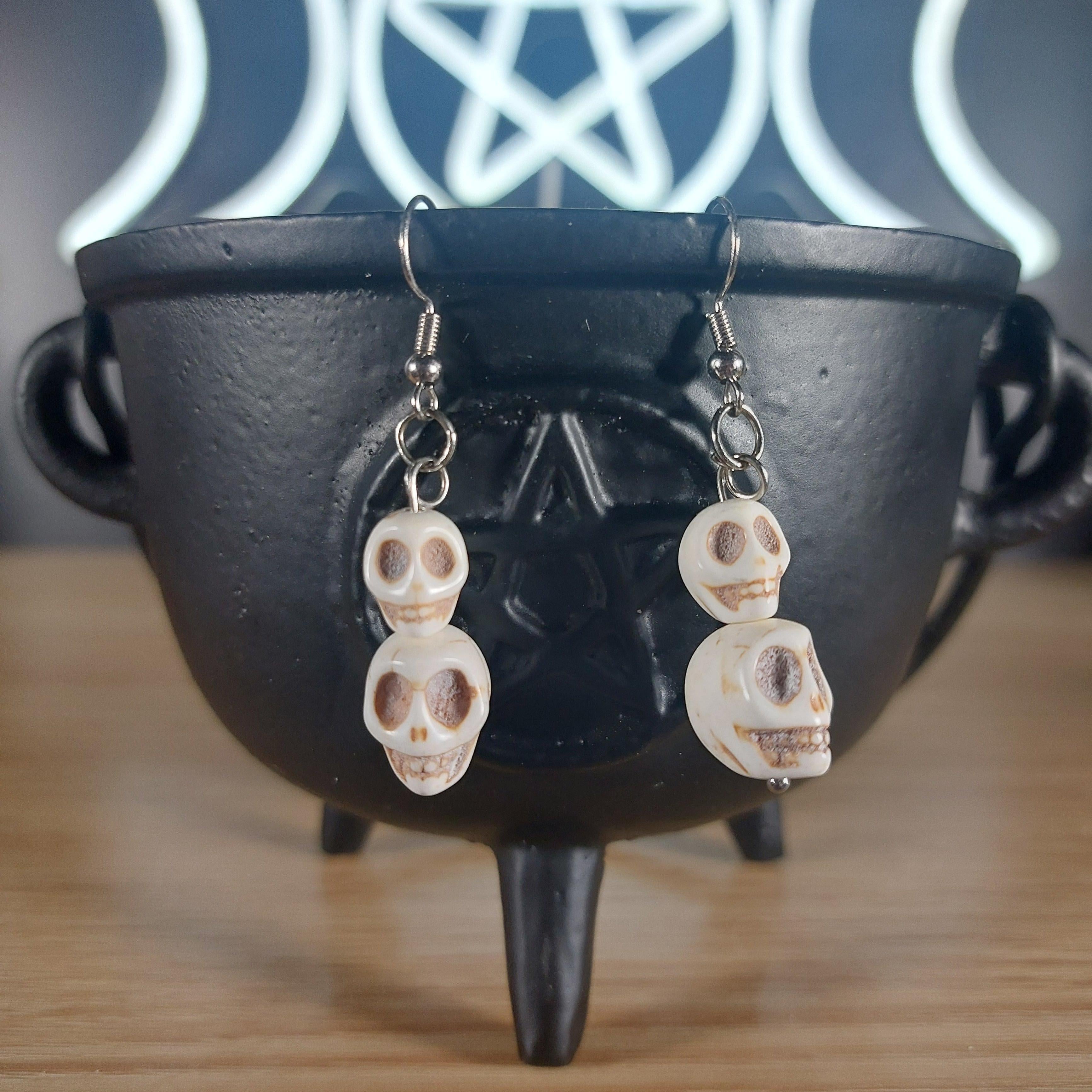 White howlite crystal skull 2-tier dangle earrings on a black cauldron.