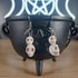 White howlite crystal skull 2-tier dangle earrings on a black cauldron.
