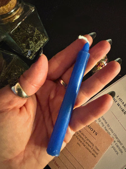 A hand holding a 4" blue taper candle
